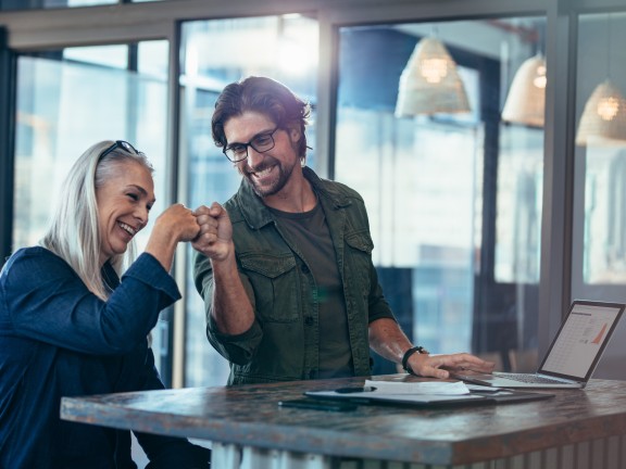 Supervisor and employee at a desk with a laptop fist bumb.