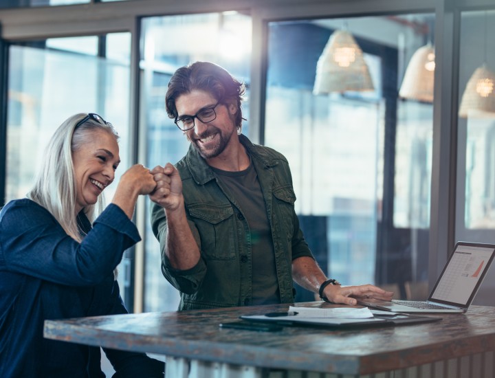 Supervisor and employee at a desk with a laptop fist bumb.